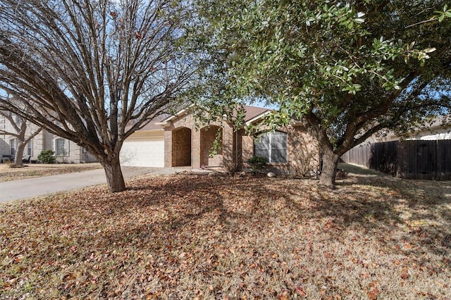 view of property hidden behind natural elements featuring a garage, driveway, and fence