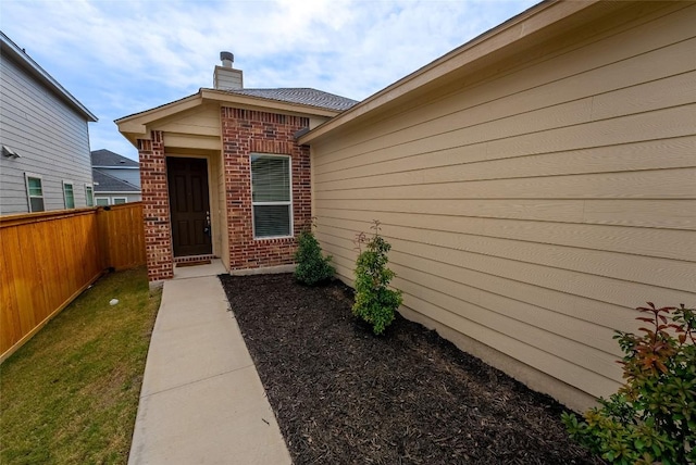 entrance to property featuring brick siding, a chimney, and fence