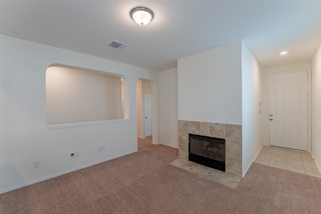 unfurnished living room with visible vents, baseboards, carpet floors, a fireplace, and arched walkways