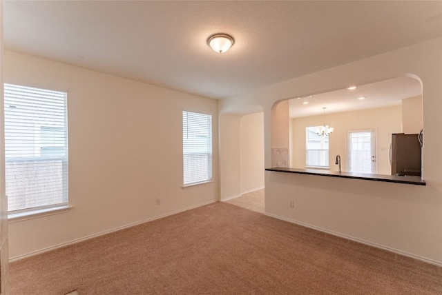 spare room featuring arched walkways, plenty of natural light, light colored carpet, and a notable chandelier