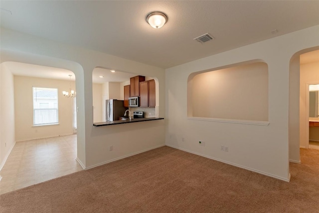 unfurnished living room with visible vents, baseboards, light colored carpet, and a chandelier