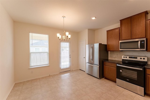 kitchen with dark countertops, appliances with stainless steel finishes, brown cabinetry, baseboards, and a chandelier