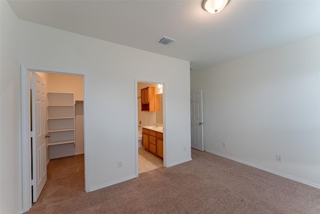 unfurnished bedroom featuring a spacious closet, baseboards, visible vents, and light carpet