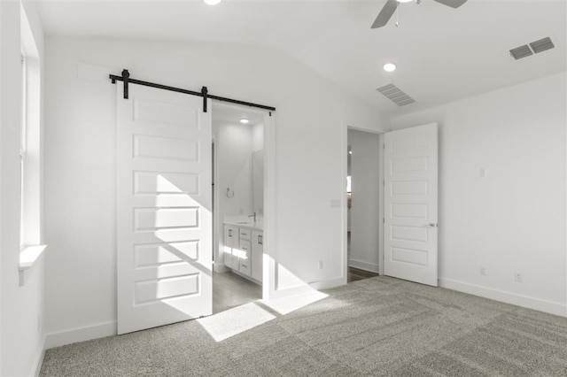 unfurnished bedroom featuring a barn door, visible vents, lofted ceiling, and light carpet