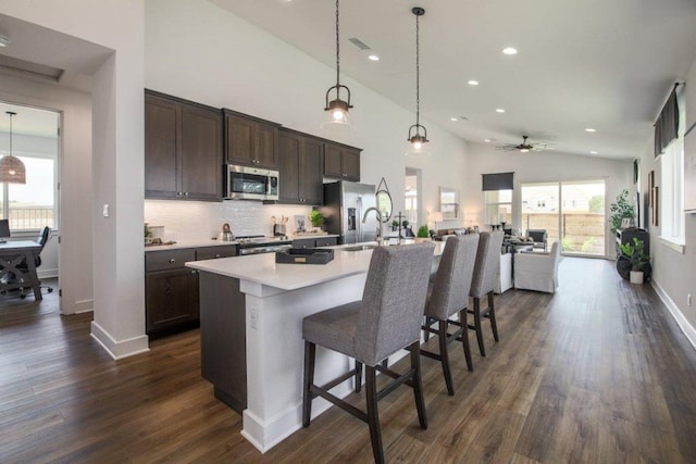 kitchen with a breakfast bar area, dark wood finished floors, dark brown cabinetry, appliances with stainless steel finishes, and backsplash