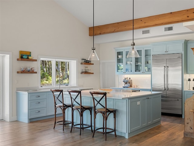 kitchen featuring visible vents, beam ceiling, open shelves, built in fridge, and a center island