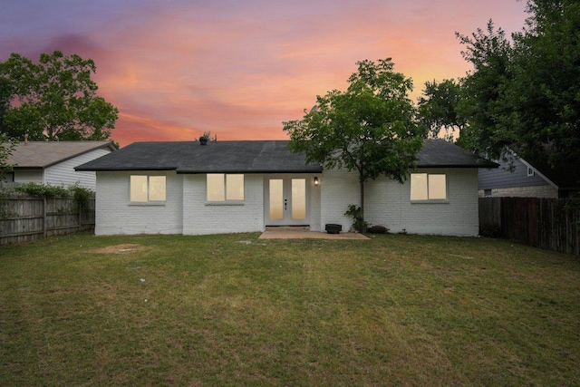 back of house at dusk featuring brick siding, a lawn, and a fenced backyard