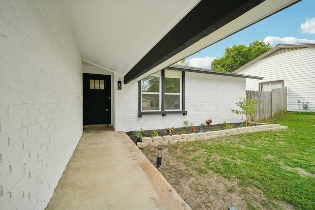 doorway to property with brick siding, a lawn, and fence