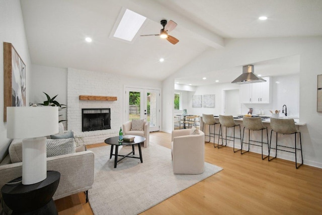 living room with a ceiling fan, recessed lighting, lofted ceiling with skylight, a brick fireplace, and light wood-type flooring