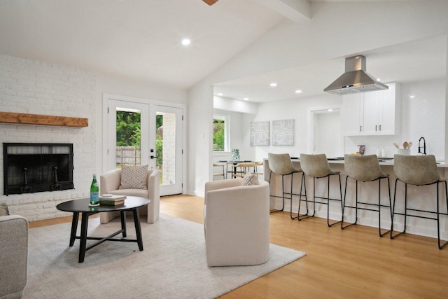 living room featuring light wood-type flooring, a brick fireplace, french doors, and vaulted ceiling