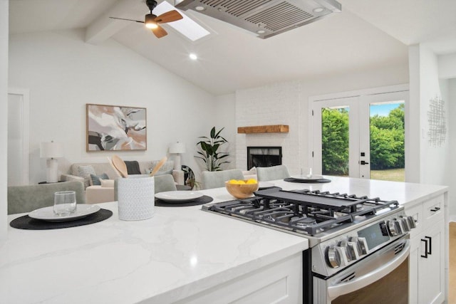 kitchen with lofted ceiling with skylight, stainless steel range with gas cooktop, open floor plan, and white cabinetry