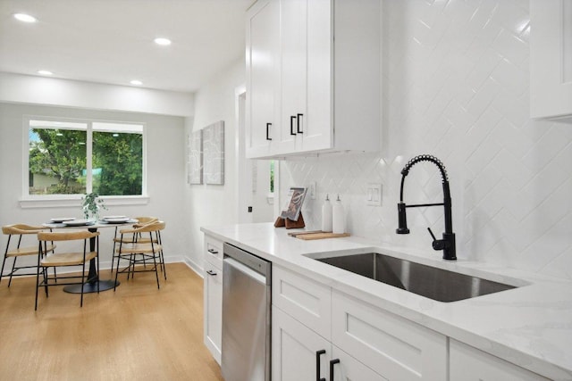 kitchen featuring a sink, light stone counters, backsplash, light wood finished floors, and dishwasher