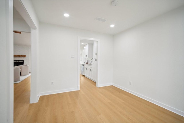 empty room featuring recessed lighting, a brick fireplace, light wood-type flooring, and baseboards