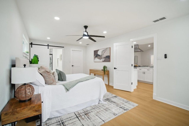 bedroom with baseboards, visible vents, recessed lighting, a barn door, and light wood-type flooring