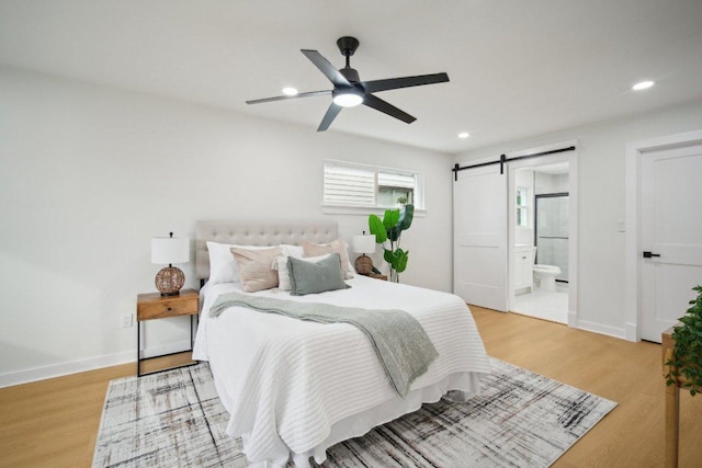 bedroom with a barn door, light wood-style flooring, recessed lighting, and baseboards