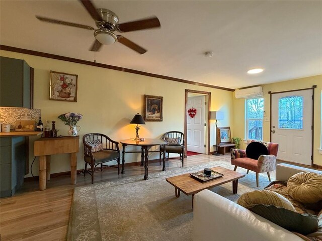 living area with baseboards, a wall unit AC, ornamental molding, wood finished floors, and a ceiling fan