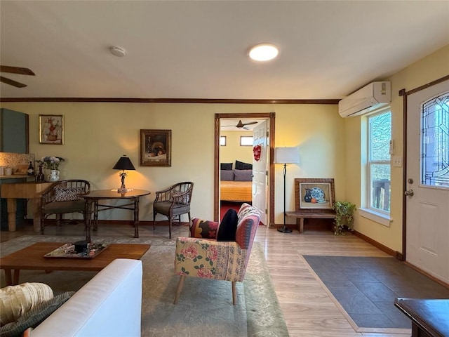 living area featuring a ceiling fan, wood finished floors, baseboards, ornamental molding, and an AC wall unit