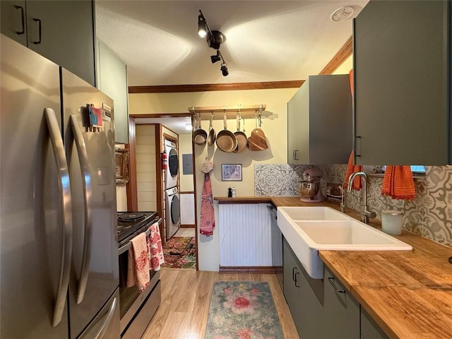 kitchen featuring light wood finished floors, a sink, stainless steel appliances, stacked washer and dryer, and wood counters