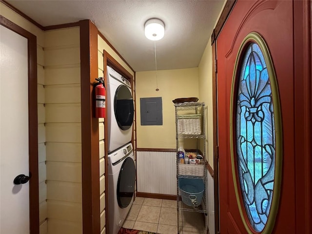 laundry room with a wainscoted wall, electric panel, laundry area, light tile patterned floors, and stacked washer / drying machine