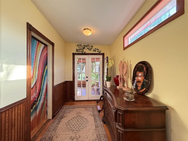 doorway with wood finished floors, wooden walls, french doors, and wainscoting