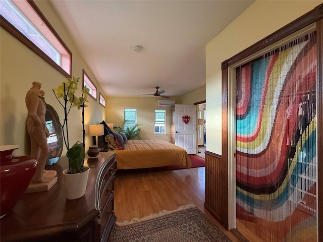 bedroom featuring ceiling fan, a wall unit AC, and wood finished floors