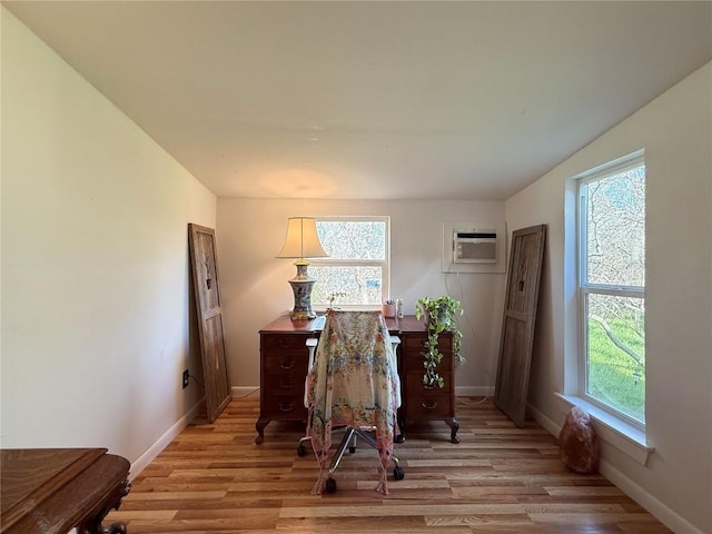 office with light wood finished floors, an AC wall unit, and baseboards