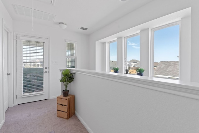 hall with visible vents, baseboards, light colored carpet, and attic access