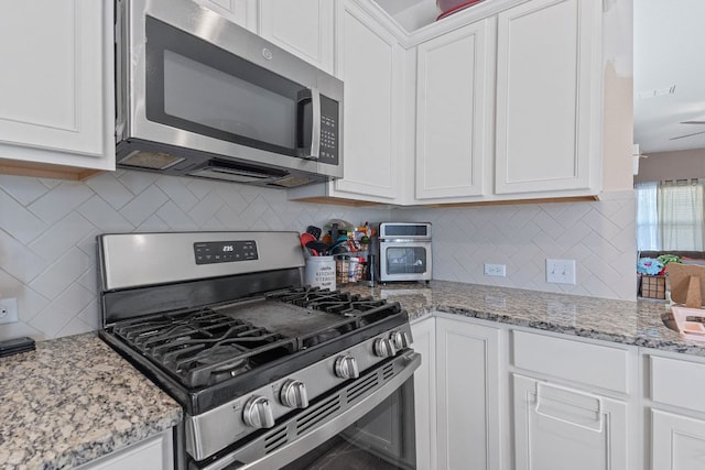 kitchen featuring white cabinets, backsplash, light stone countertops, and appliances with stainless steel finishes