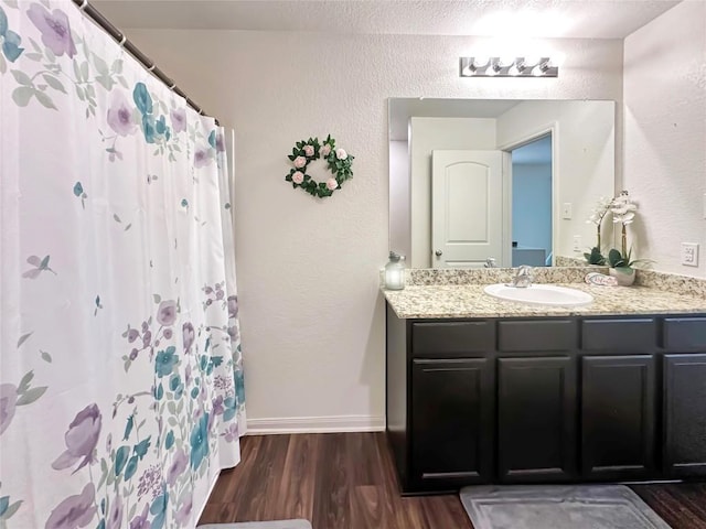 full bath featuring curtained shower, baseboards, wood finished floors, a textured wall, and vanity