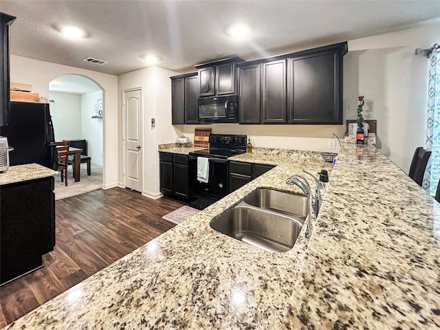 kitchen featuring dark wood-type flooring, black appliances, a sink, arched walkways, and light stone countertops