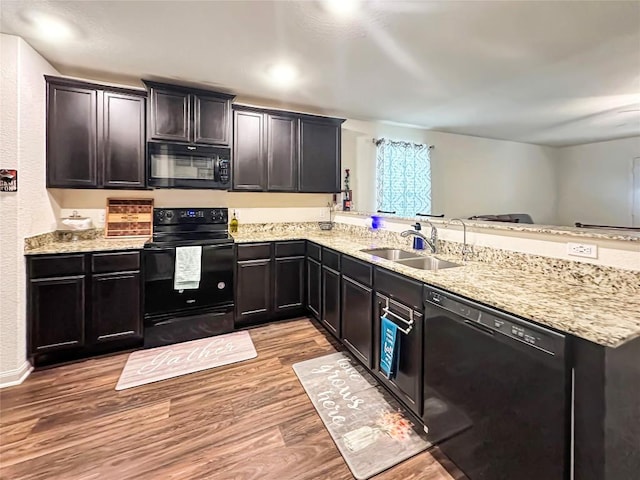 kitchen with black appliances, a sink, light wood-style floors, a peninsula, and light stone countertops