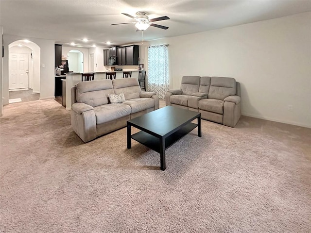 living area featuring a ceiling fan, light colored carpet, arched walkways, and baseboards