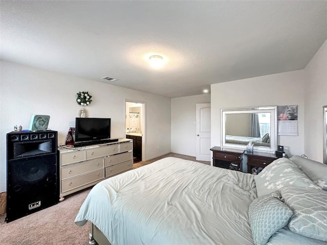 bedroom featuring visible vents, baseboards, light colored carpet, and ensuite bathroom