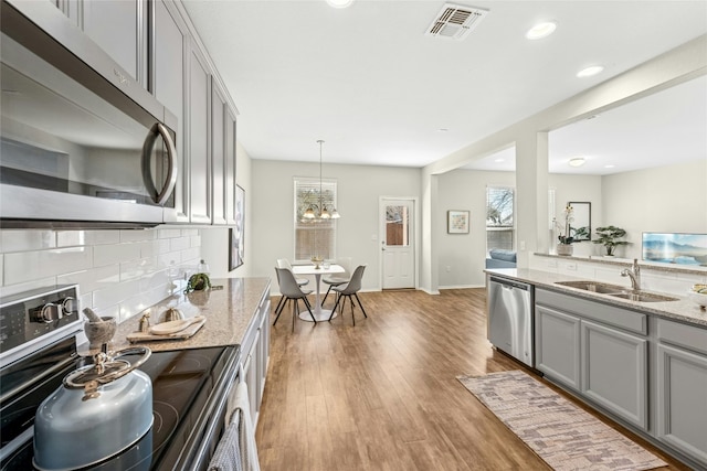 10407 Abana Way, Austin, TX 78748 - kitchen with stainless steel appliances, decorative backsplash, gray cabinets, light stone countertops, and a chandelier