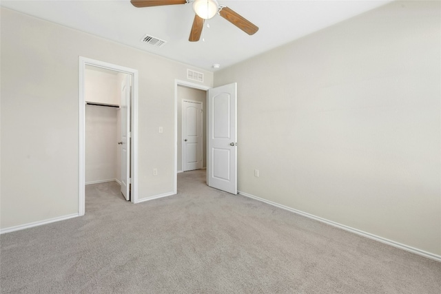 unfurnished bedroom with a walk in closet, baseboards, visible vents, and light carpet