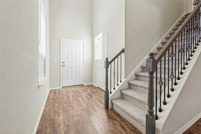 foyer with stairs, a high ceiling, baseboards, and wood finished floors