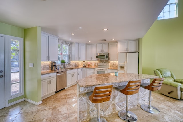 kitchen with a sink, light stone counters, backsplash, stainless steel appliances, and white cabinets