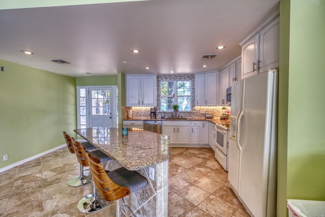 kitchen featuring light stone countertops, a breakfast bar area, decorative backsplash, plenty of natural light, and stainless steel appliances