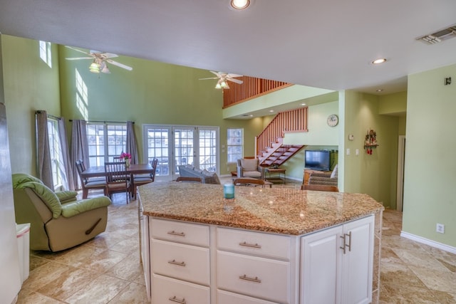 kitchen featuring light stone countertops, visible vents, a towering ceiling, white cabinetry, and open floor plan