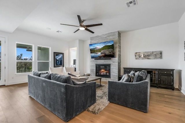 living area featuring visible vents, a large fireplace, baseboards, and wood finished floors