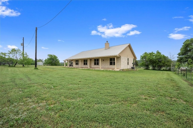 back of house featuring a chimney, metal roof, a yard, and fence