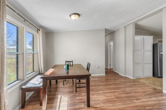 dining space featuring baseboards, visible vents, a textured ceiling, and light wood-style floors