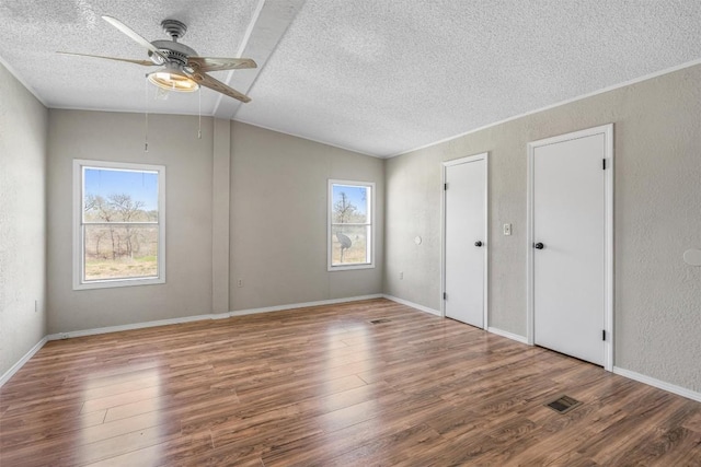 unfurnished bedroom featuring visible vents, wood finished floors, vaulted ceiling, and a textured wall