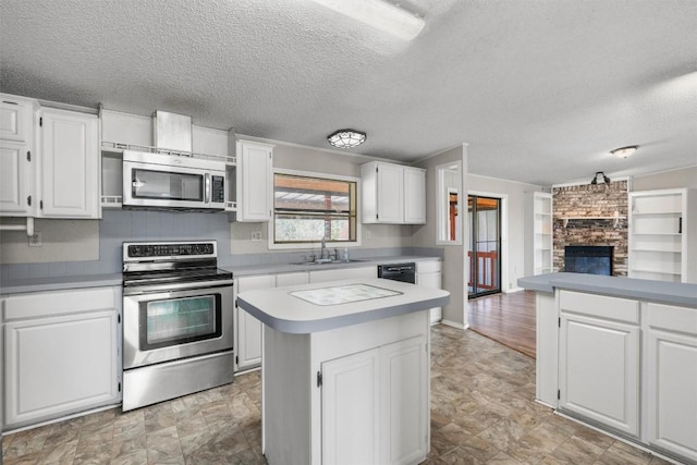 172 Hershal Ln, Cedar Creek, TX 78612 - kitchen featuring appliances with stainless steel finishes, a textured ceiling, a large fireplace, open floor plan, and white cabinets