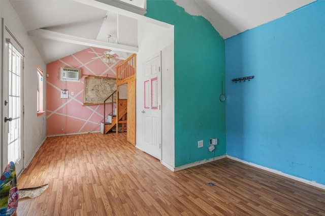 empty room with a wall unit AC, wood finished floors, lofted ceiling with beams, ceiling fan, and stairs