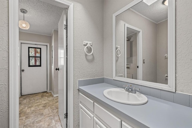 bathroom featuring vanity, crown molding, a textured wall, and a textured ceiling