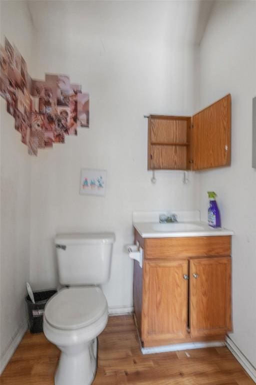 half bath with vanity, toilet, wood finished floors, and baseboards