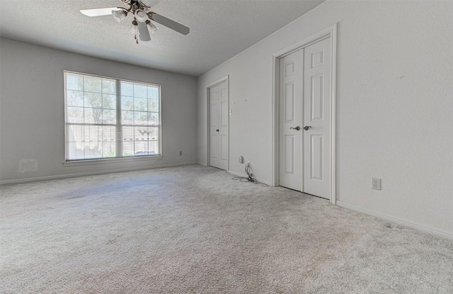 unfurnished bedroom with a ceiling fan, carpet, baseboards, a textured ceiling, and two closets