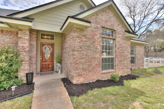 view of exterior entry with brick siding and fence