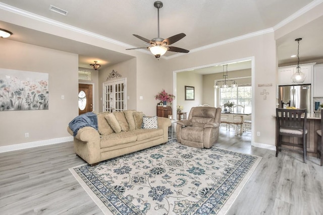 living room with visible vents, baseboards, crown molding, and light wood-style floors